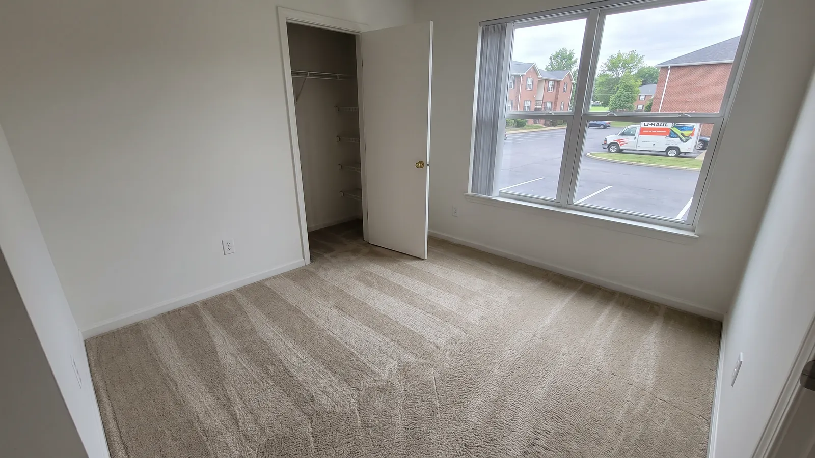 Empty bedroom in a Clarksville apartment with freshly cleaned carpet showing straight wand lines, bare walls and a window looking onto a parking lot